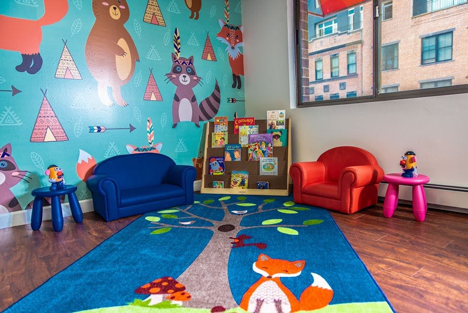 Children's play area with a blue rug, small chairs, and a bookshelf