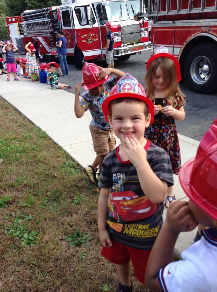 Children wearing red firefighter hats near a fire truck