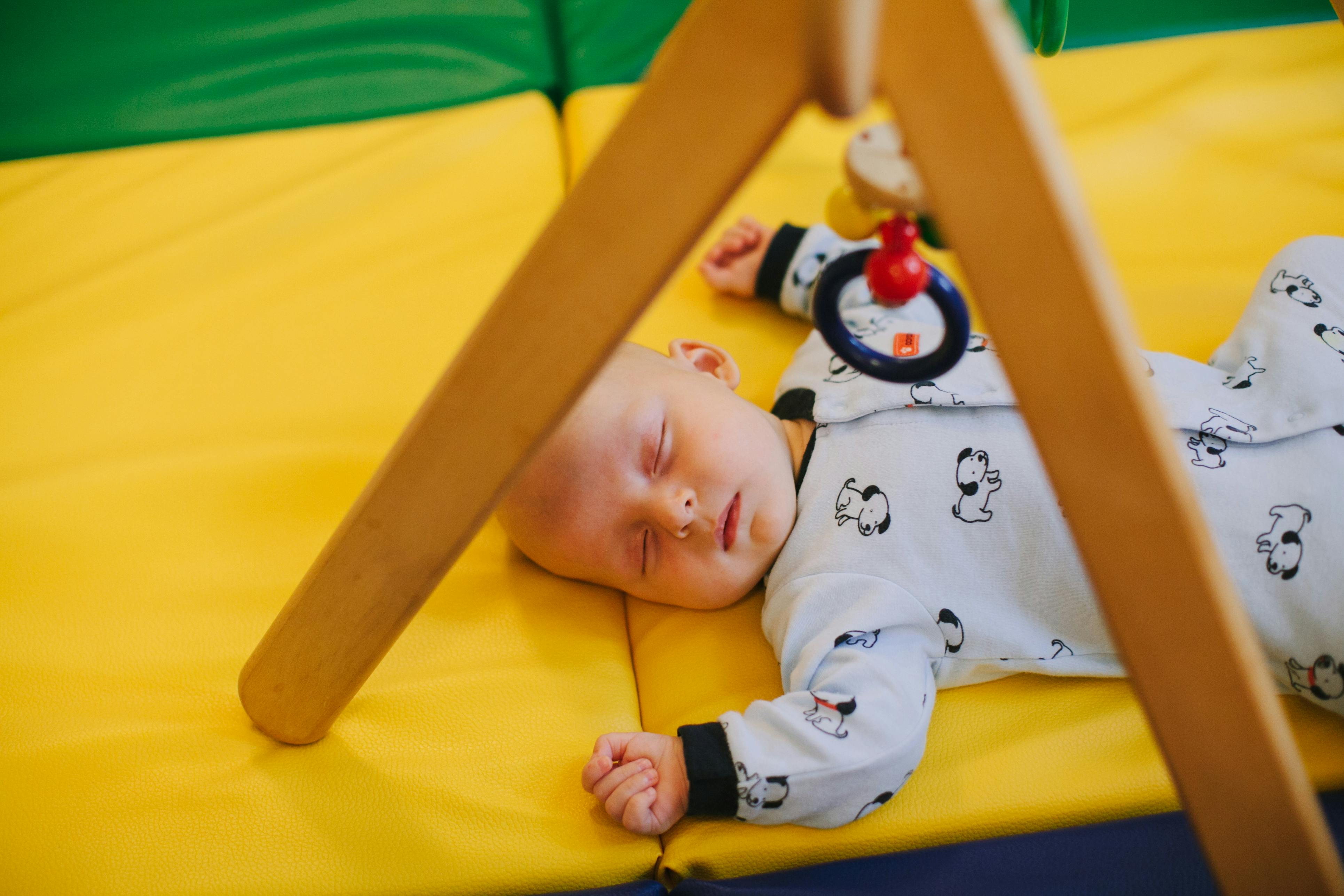 Sleeping baby on a yellow mat under a wooden play gym