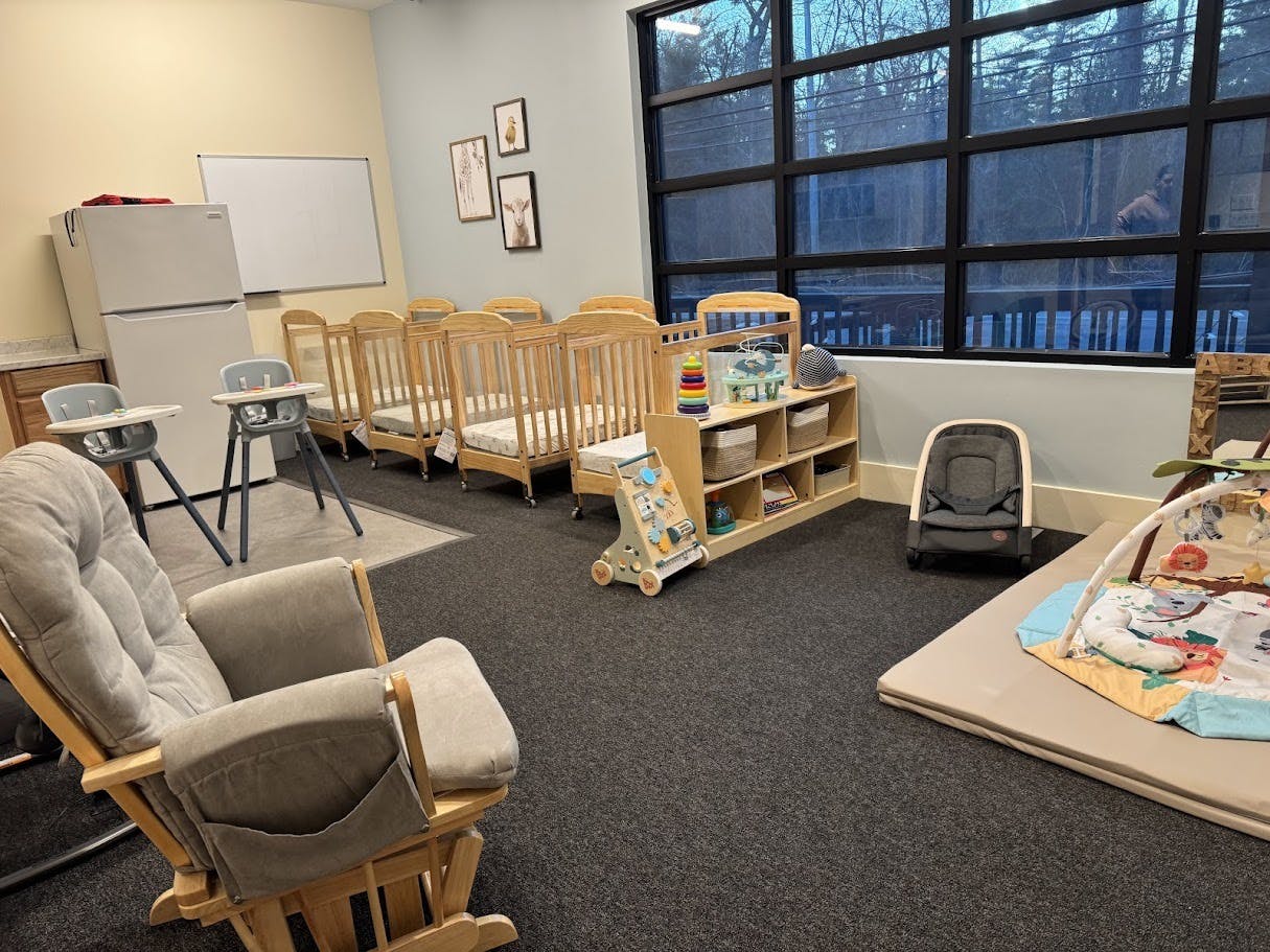 A room with several cribs, high chairs, a rocking chair, and play mats