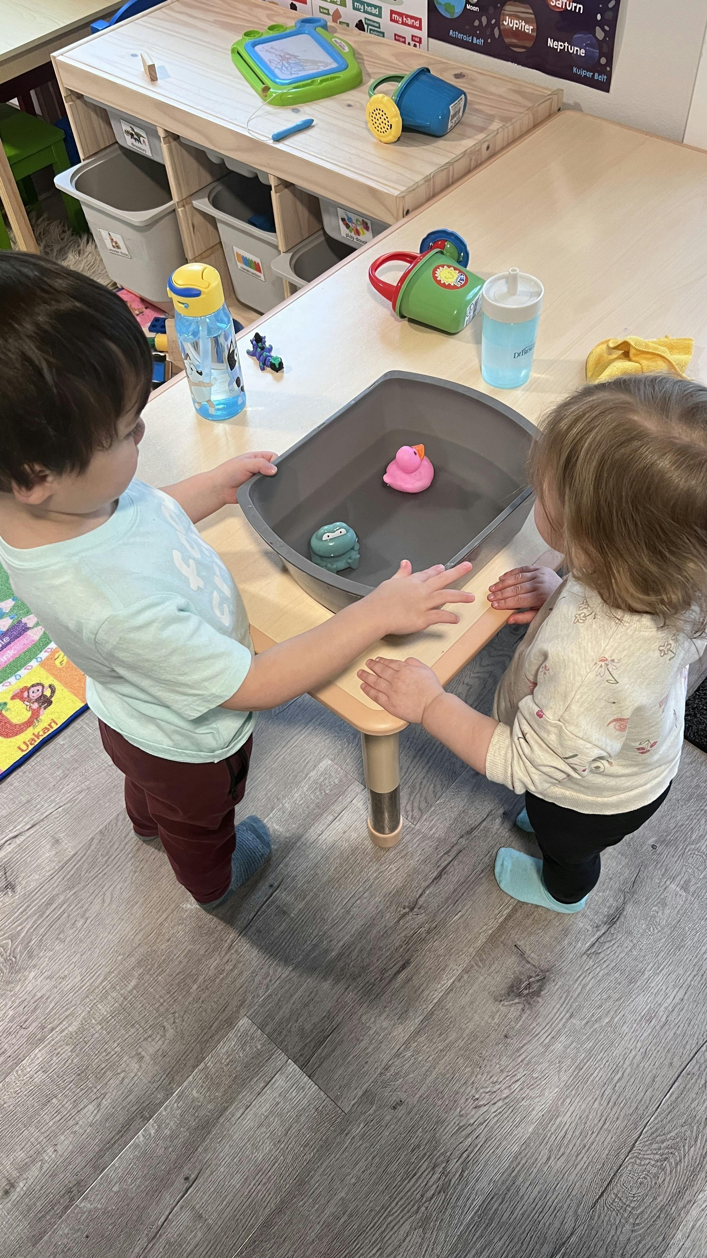 Two children playing with toy ducks in a tub of water on a small table