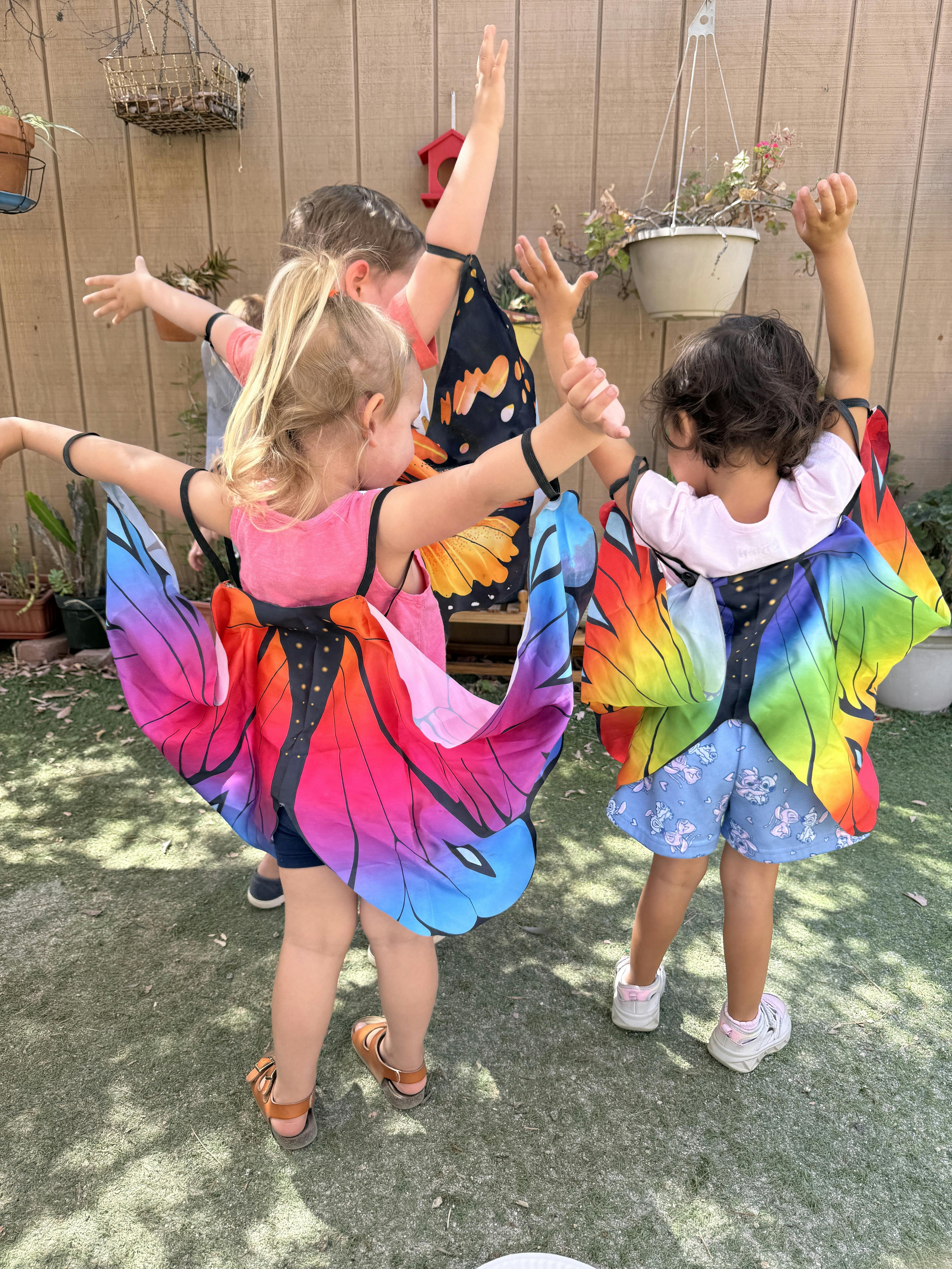 Three children wearing colorful butterfly wings with arms raised