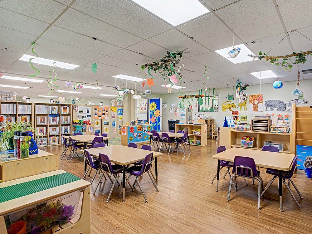 Empty classroom with small tables and chairs, shelves, and decorations