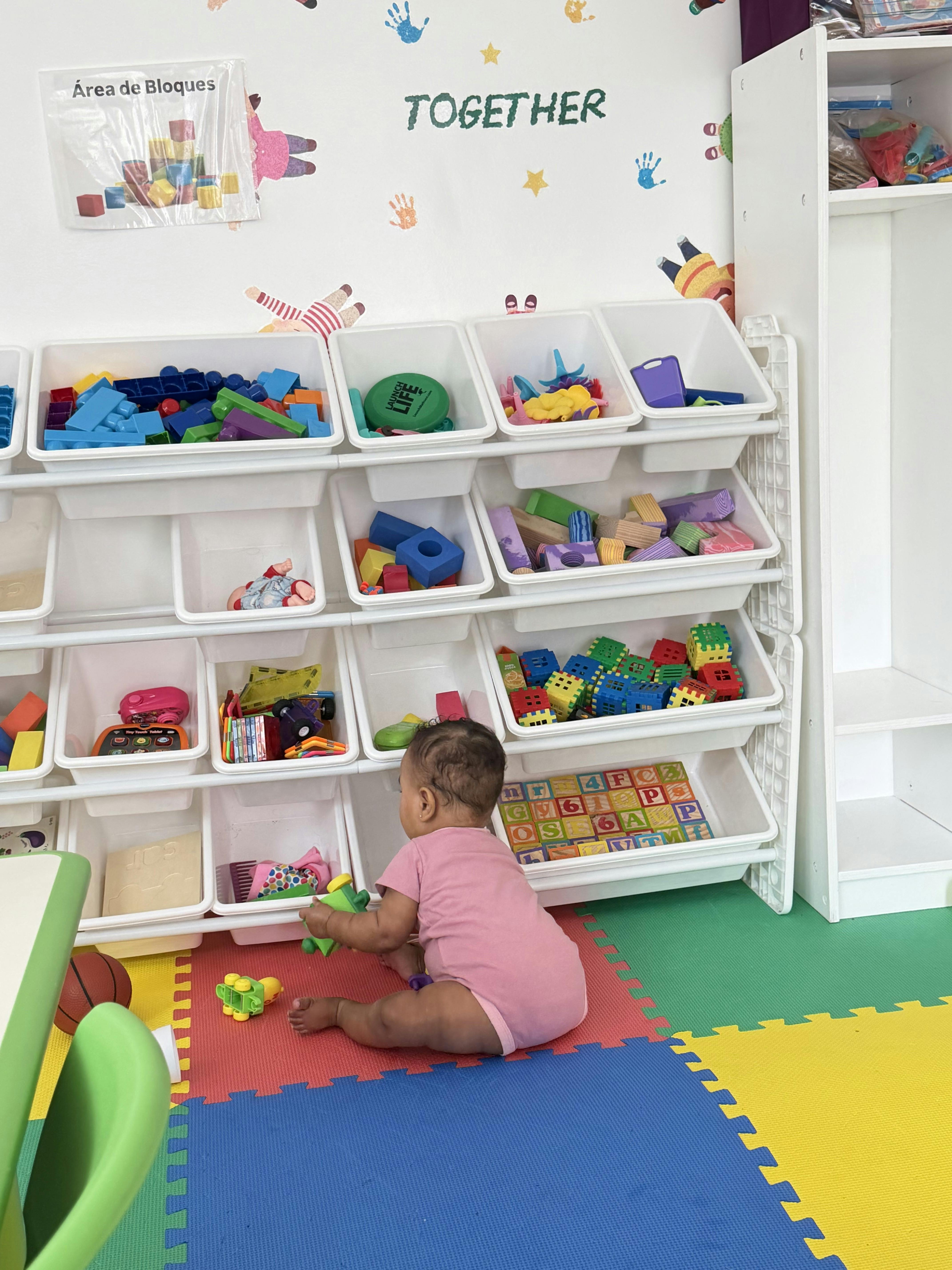 A child sitting on a colorful floor mat playing with toys near a storage unit