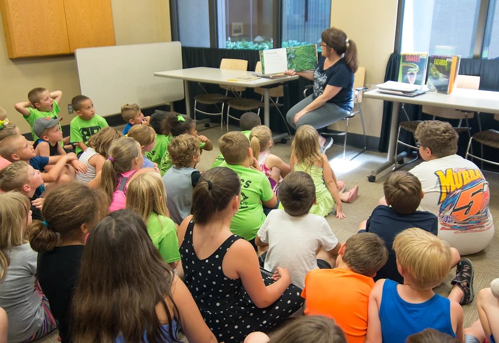 Person reading a book to a group of children sitting on the floor