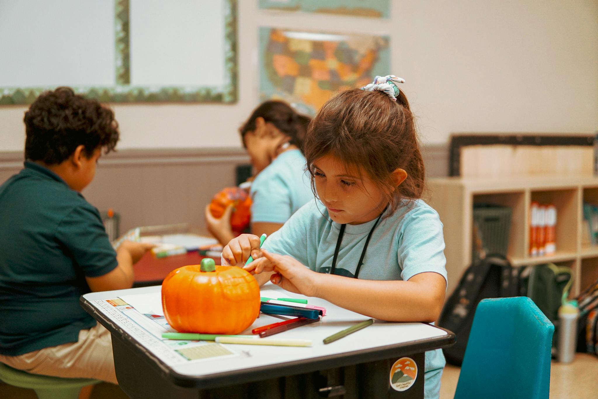 Child coloring a small decorative pumpkin at a desk in a classroom