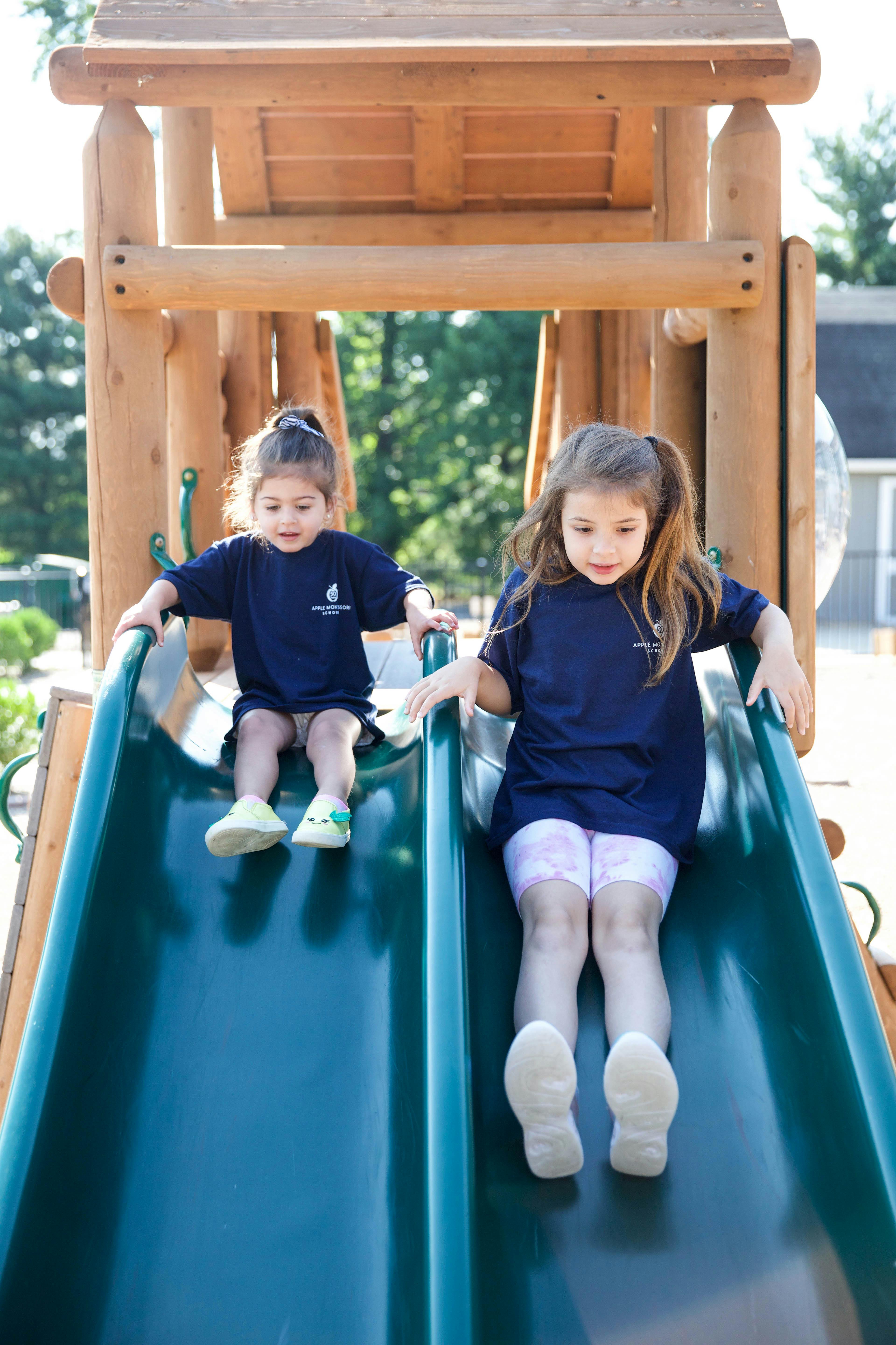 Two children in uniform sliding down a double playground slide