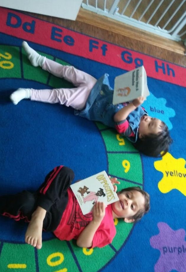 Two children lying on a rug with letters and numbers, reading books