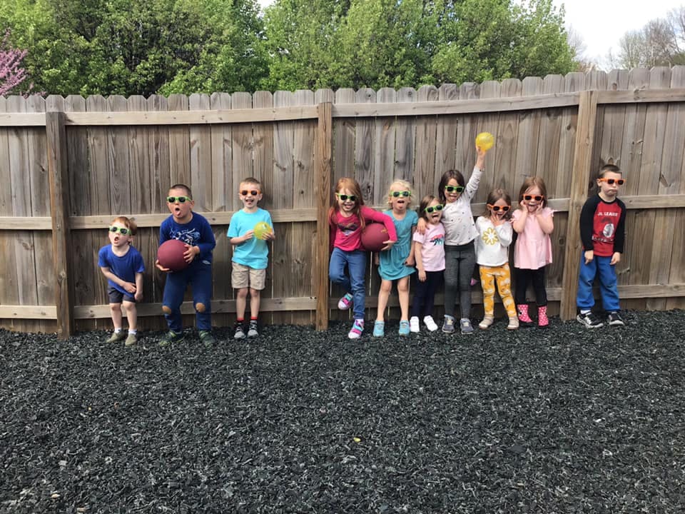 Group of children wearing sunglasses standing in front of a wooden fence