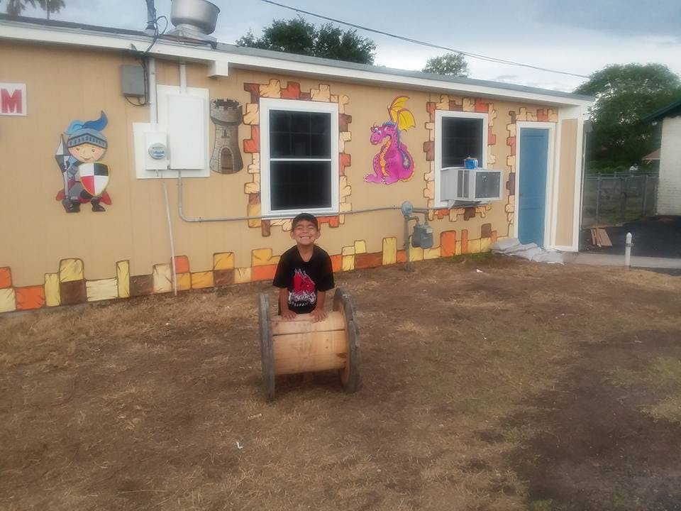 Child sitting in a wooden barrel in front of a building with murals