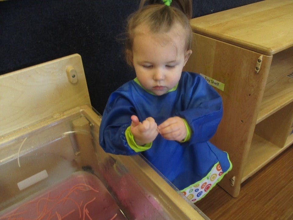 Child in a blue smock looking at their hands over a clear bin