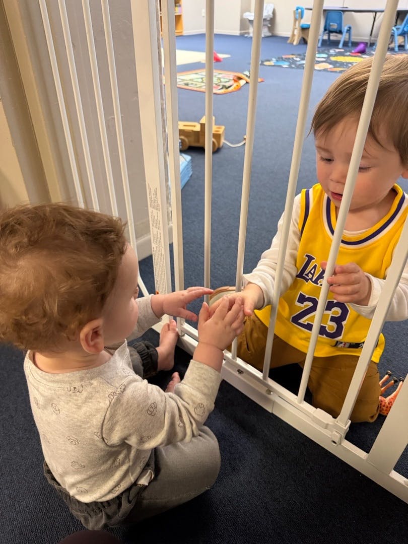 Two children reaching for each other through a baby gate in a playroom