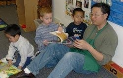 Adult reading book to three children in a classroom