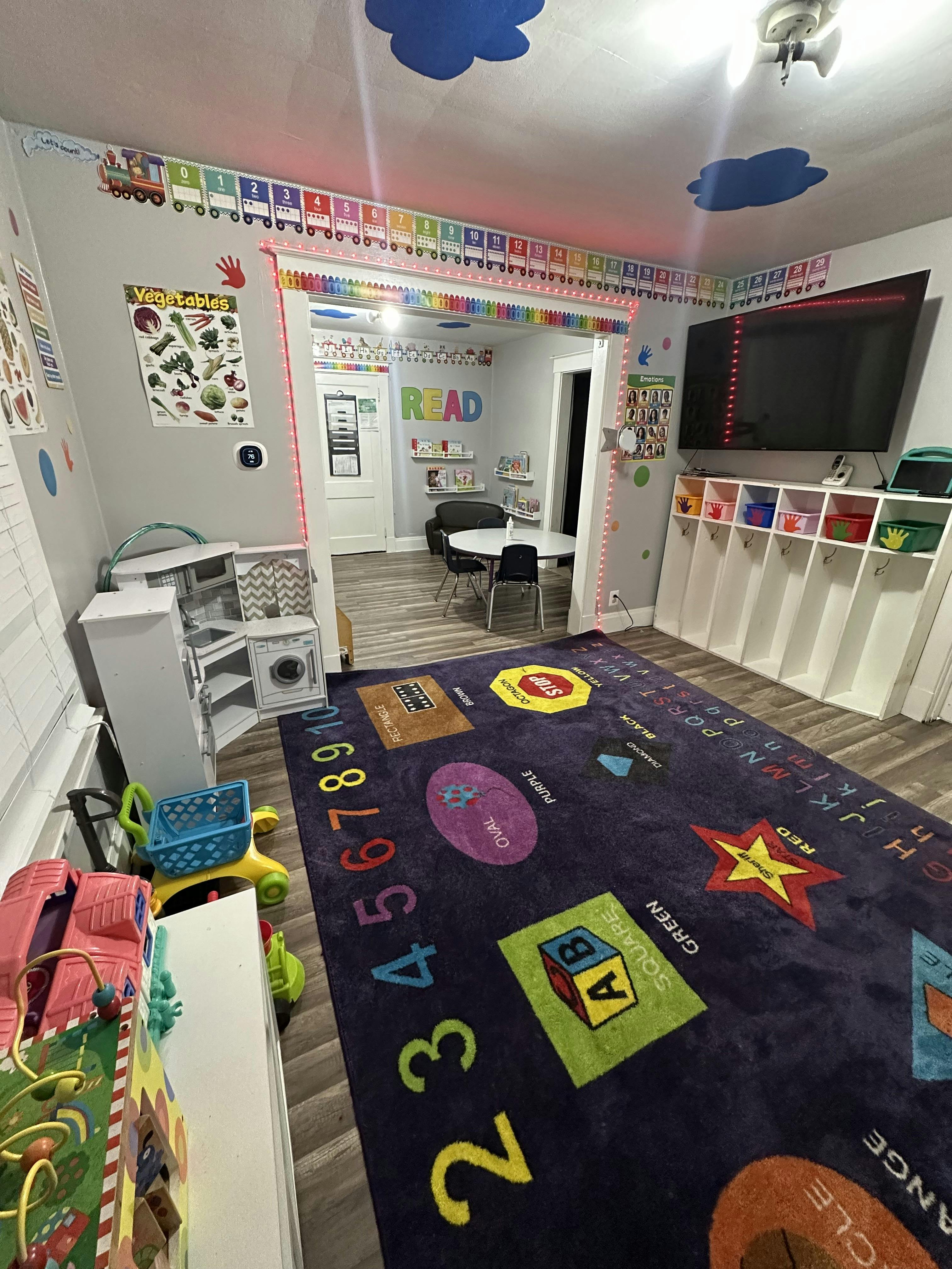 Playroom with a colorful alphabet and numbers rug, toys, and a TV