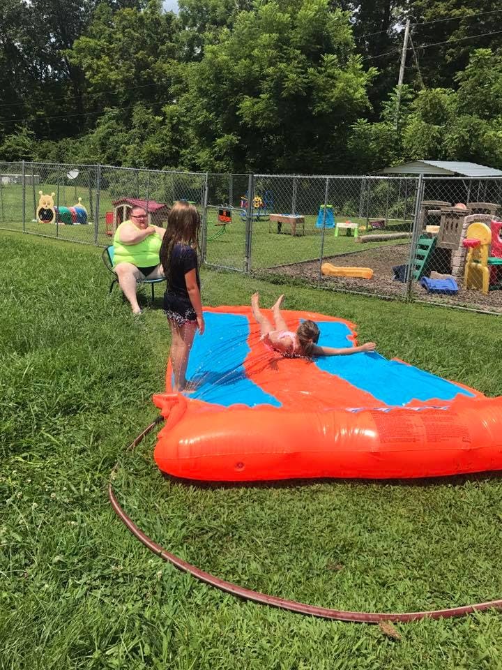 Person sitting in a chair watching two children on an inflatable water slide
