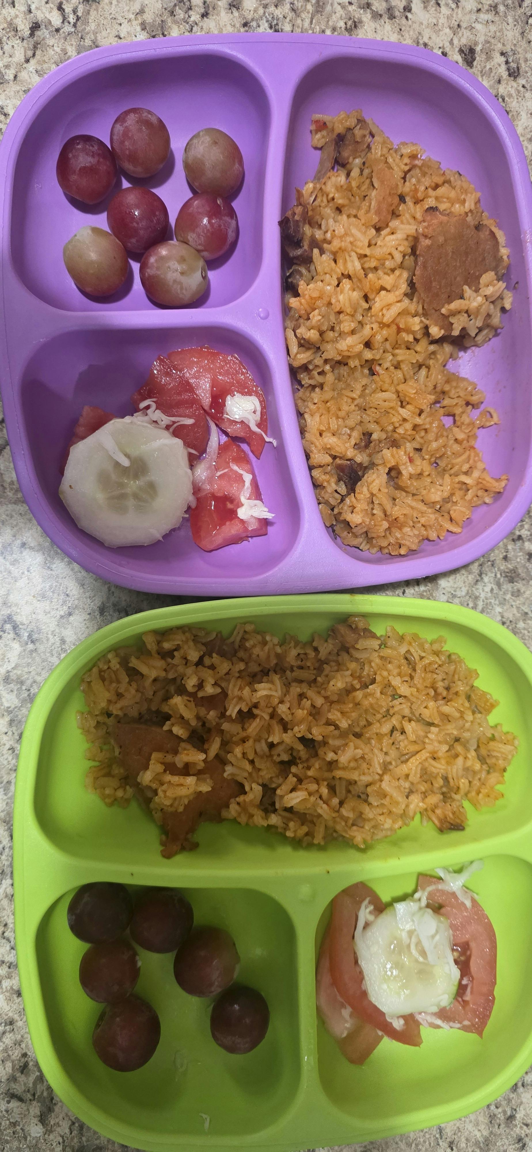 Two partitioned plates served with rice, grapes, and sliced tomato and cucumber