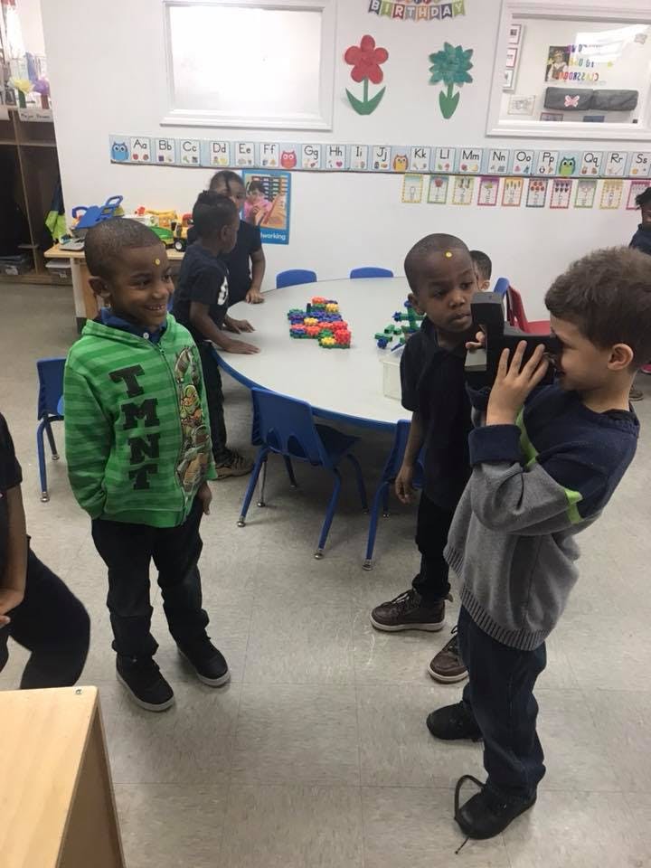 Child holding a camera-like object up to another child's face in a classroom