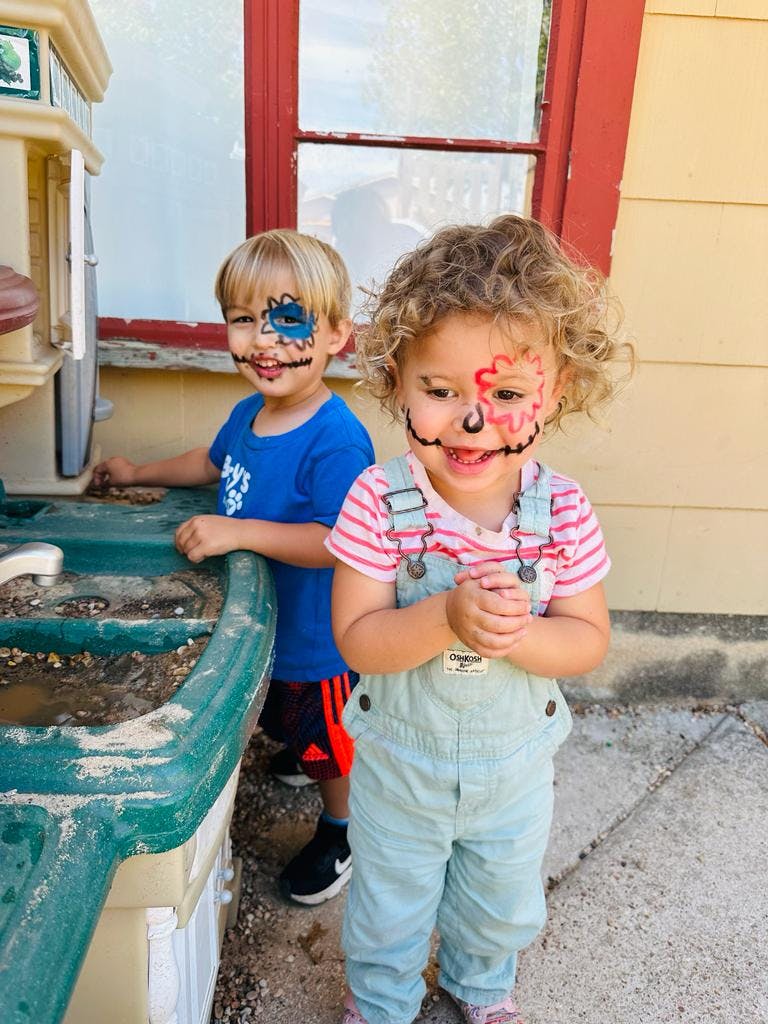 Two children with painted faces standing outdoors