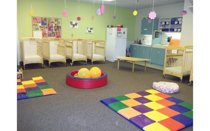 An empty nursery room with multiple cribs, a changing station, and play mats