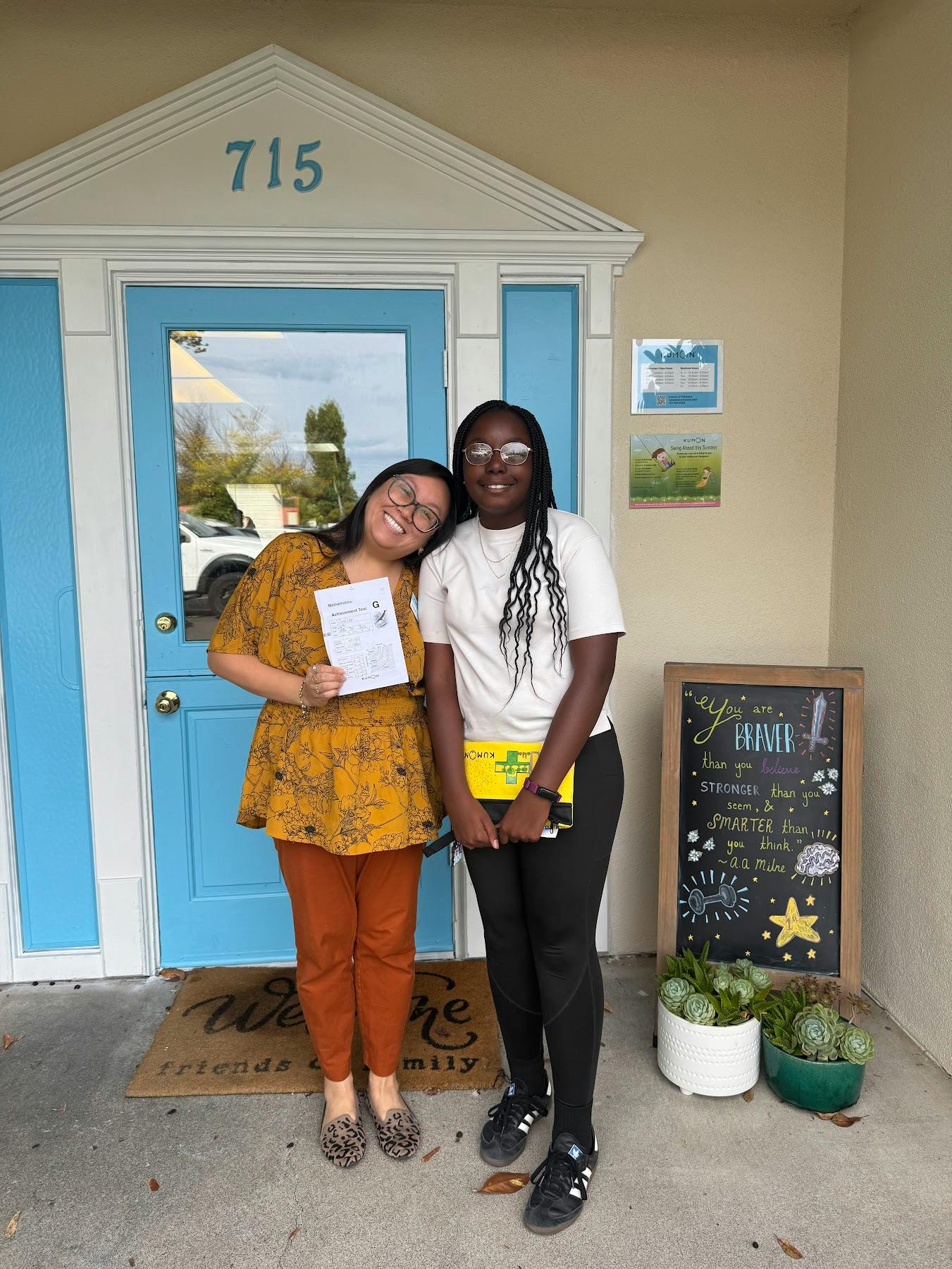 Two people standing in front of a building entrance with a chalk sign