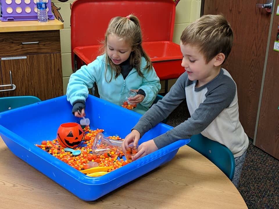 Two children playing with candy corn in a blue bin