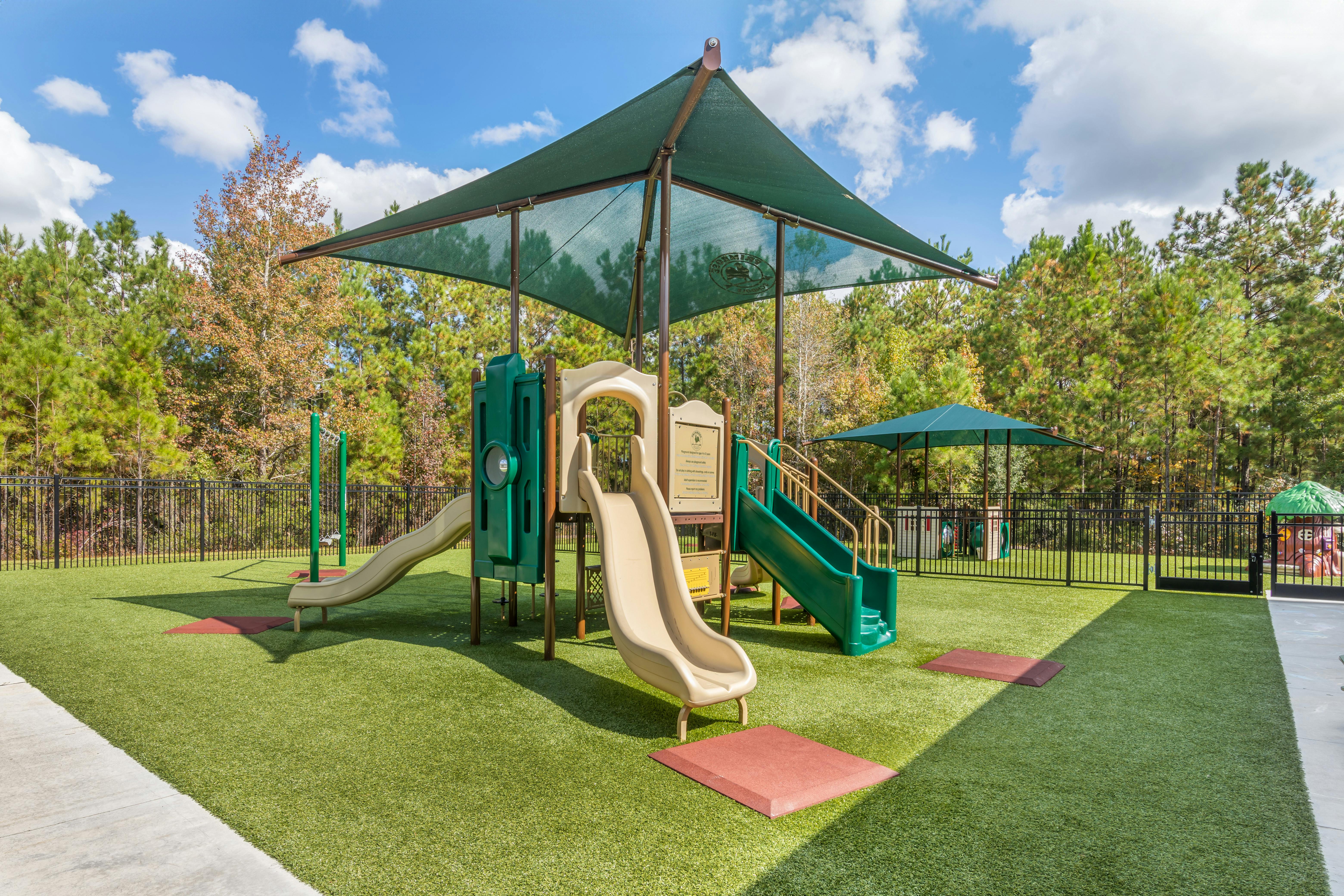 A green and tan playground with slides and a climbing structure under a shade cover
