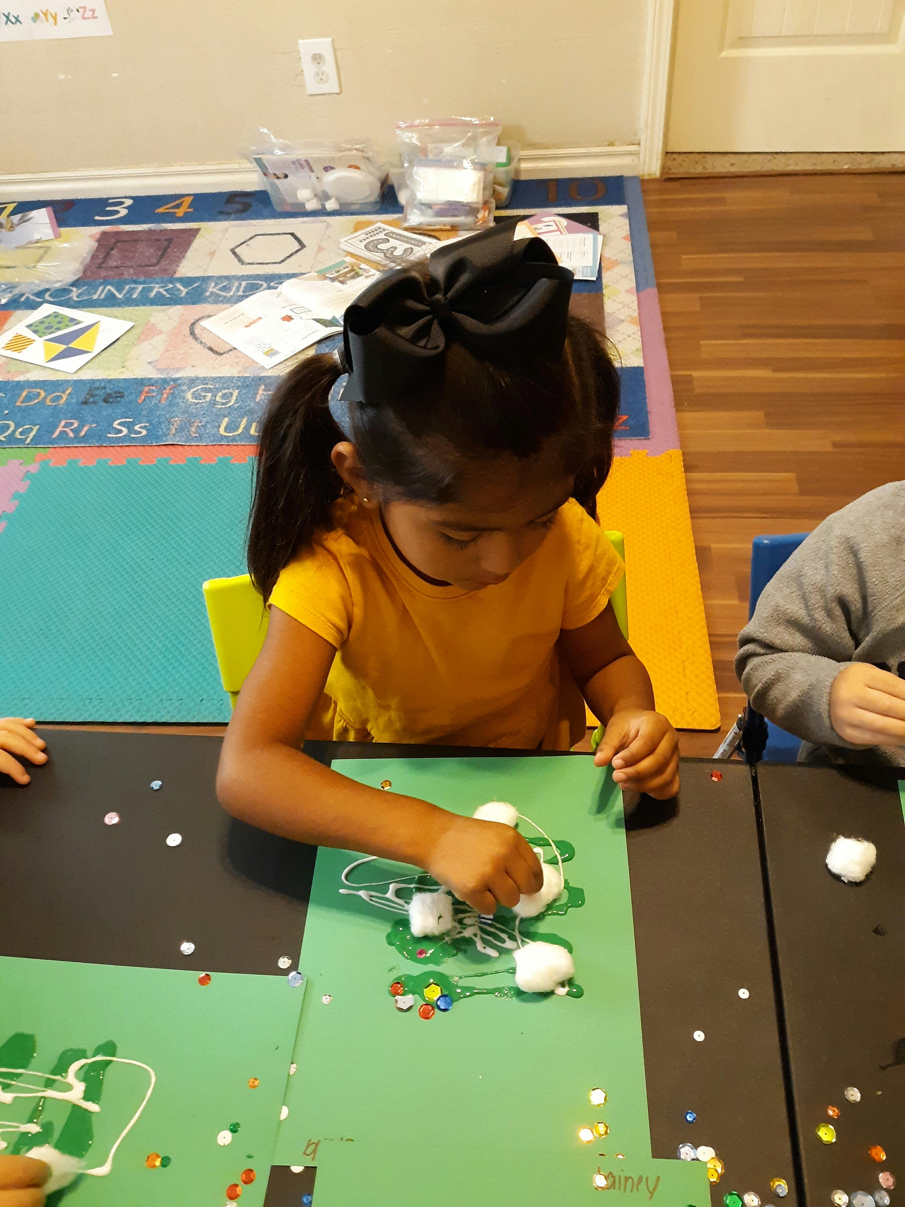 Child doing an art project with cotton balls and glue on green paper