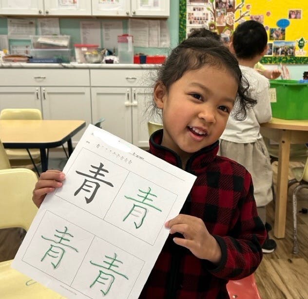Child holding up a paper with Chinese characters in a classroom