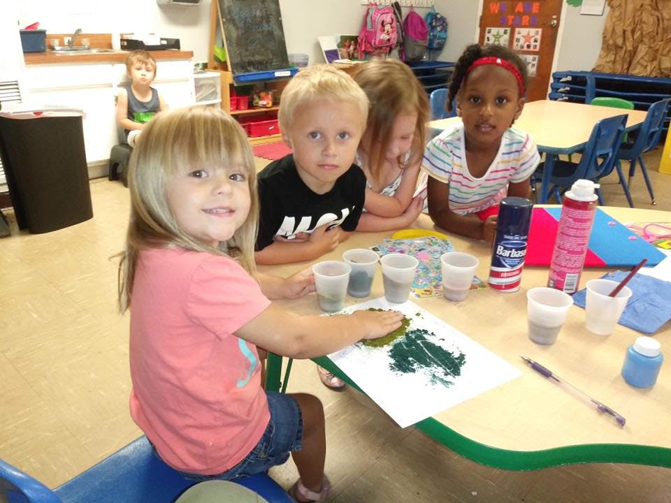 Children at a table doing an art activity with paint and cups