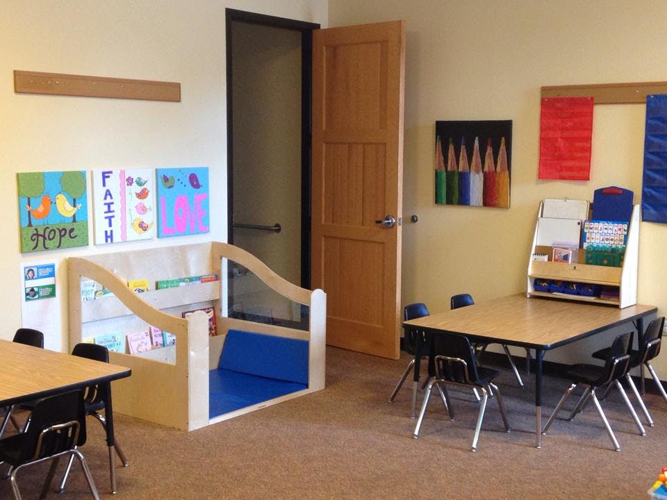 Classroom with small tables and chairs, a reading nook, and colorful artwork