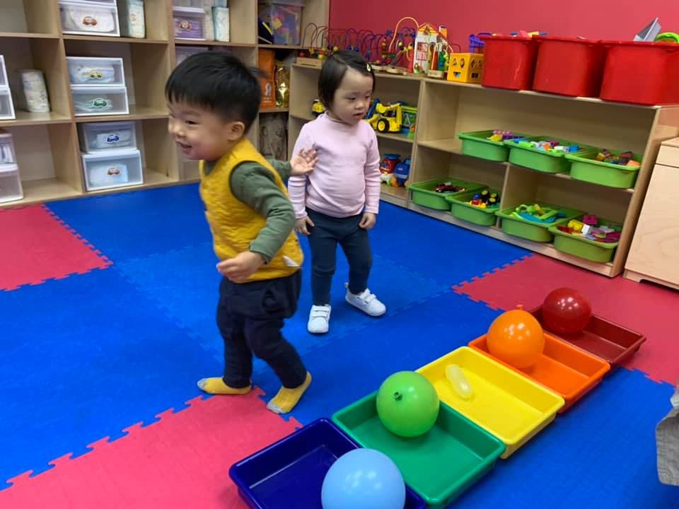 Two children playing with colorful balls and trays in a classroom