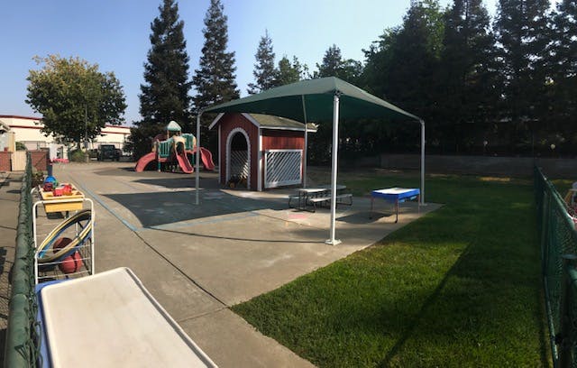 An outdoor playground with a slide set, playhouse, and shaded picnic table