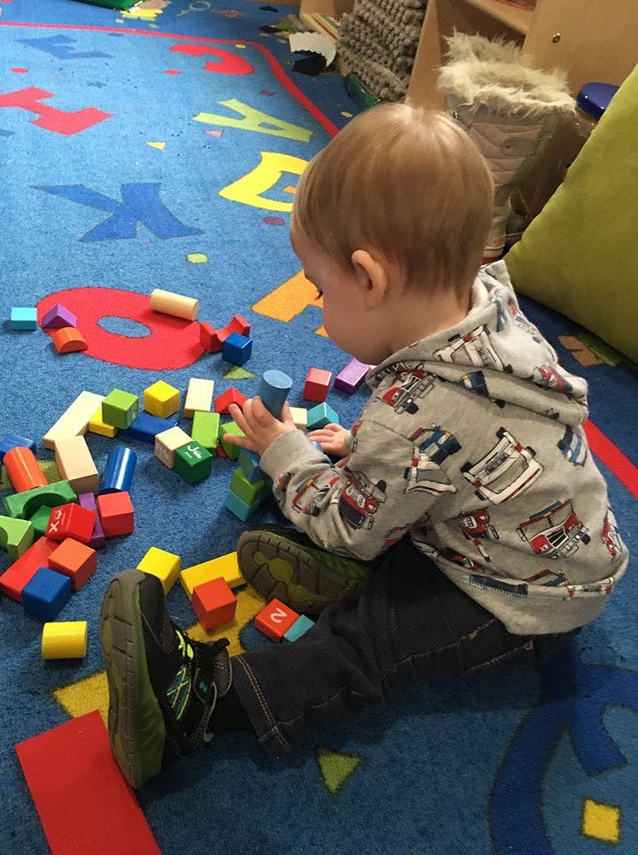 Child playing with colorful building blocks on a blue alphabet rug
