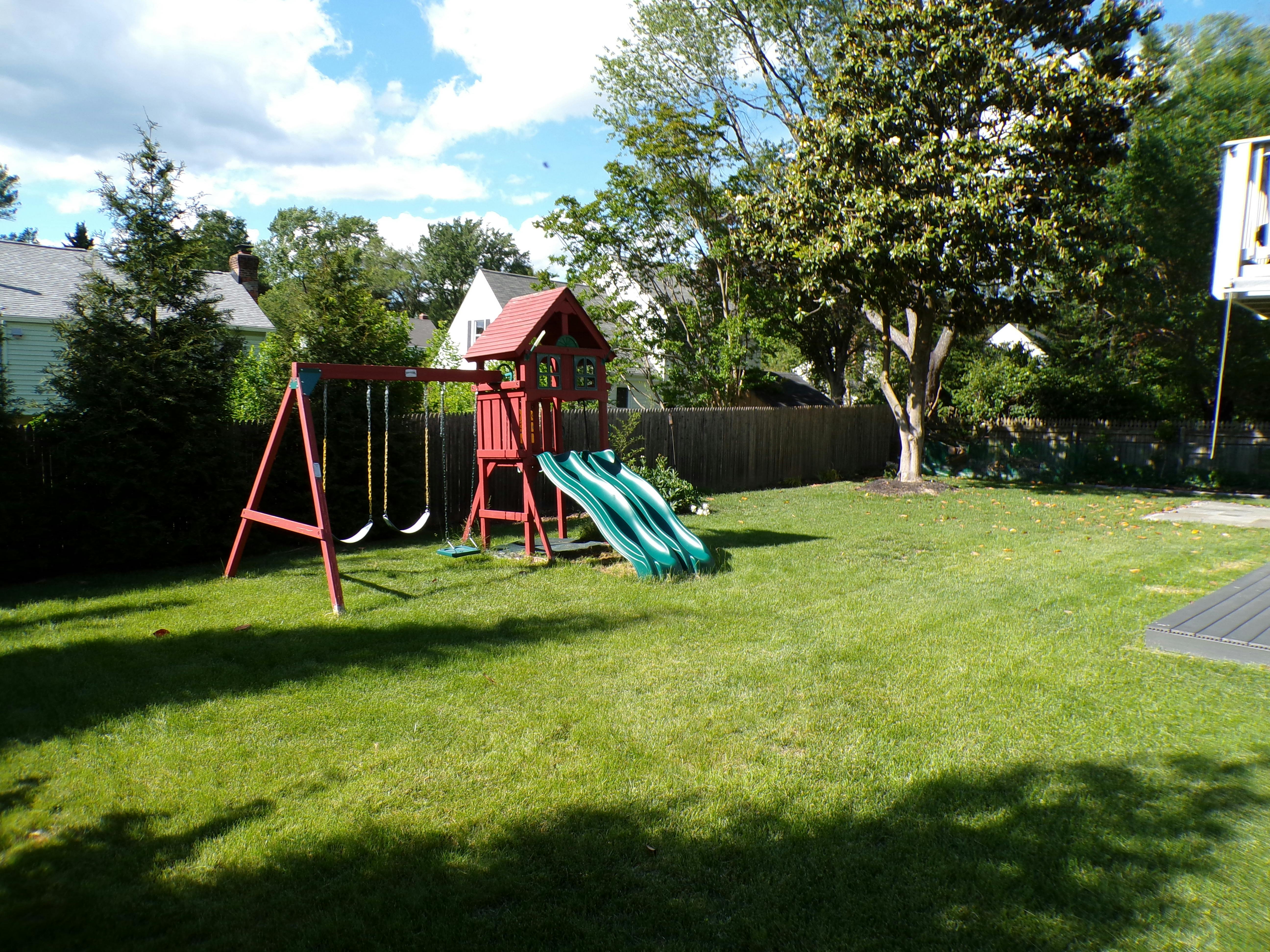 Red swing set with two swings and a green slide in a grassy yard