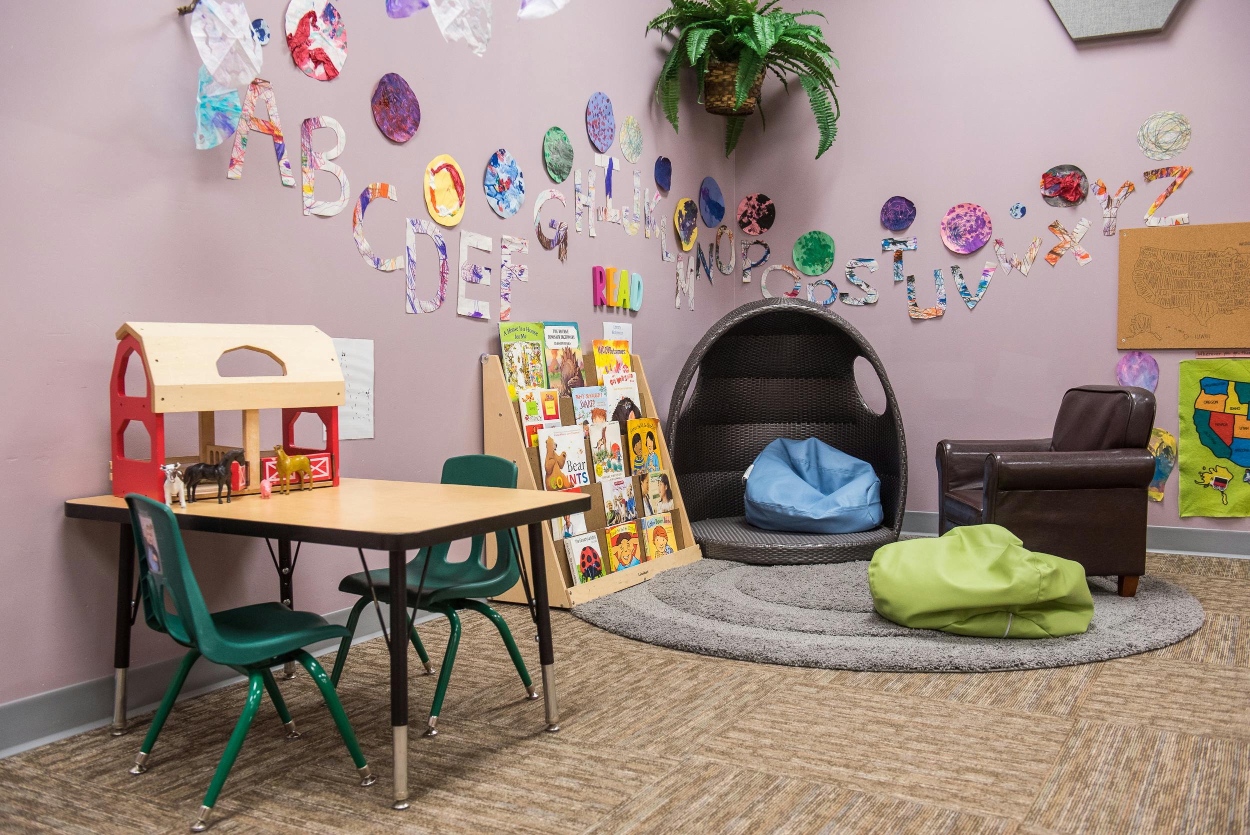 Children's play area with a table, chairs, bookshelf, and seating pods