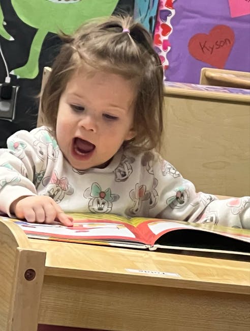 Child pointing at an open book on a wooden desk