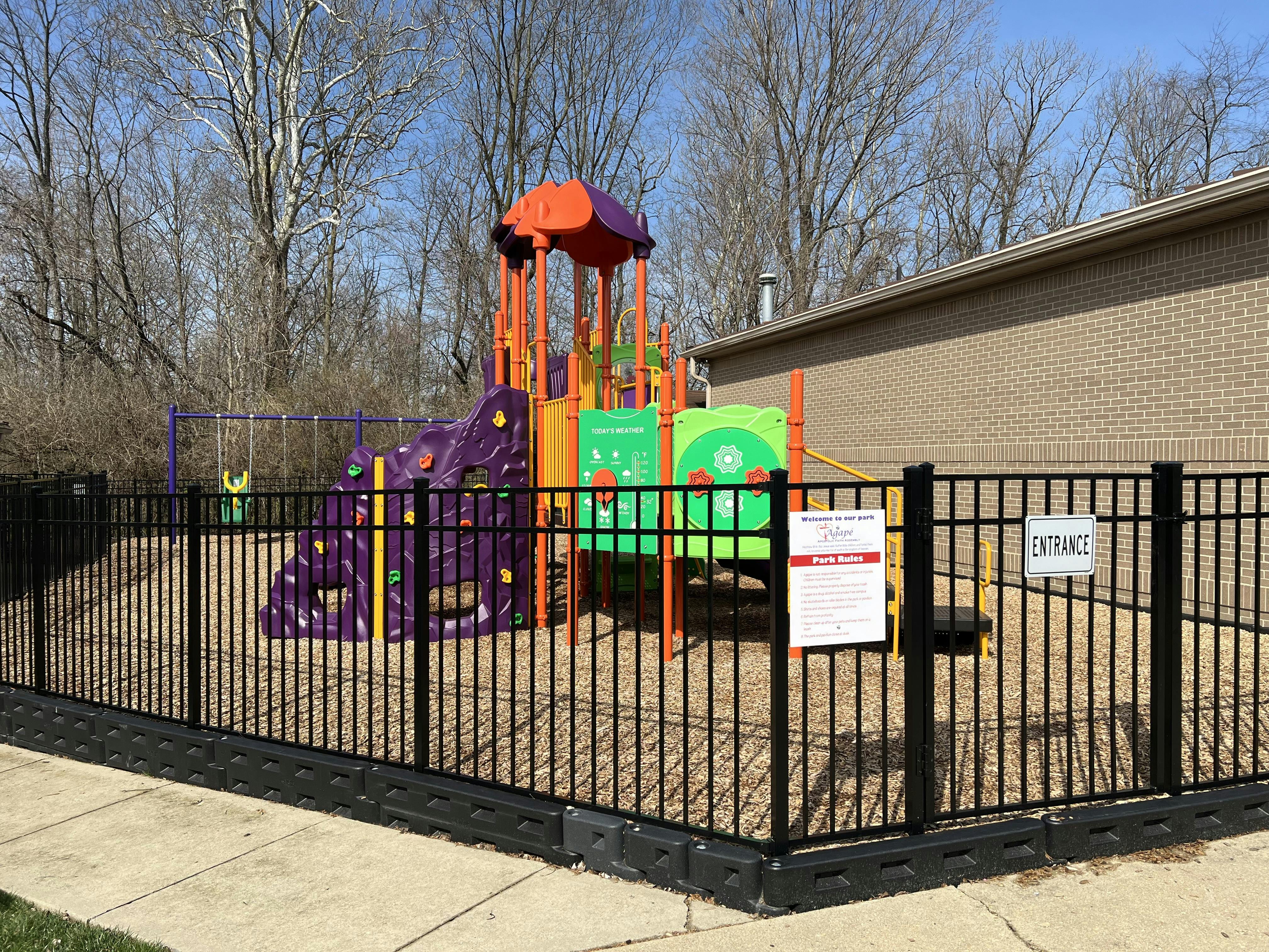 Playground with colorful climbing structure and swings behind a black fence