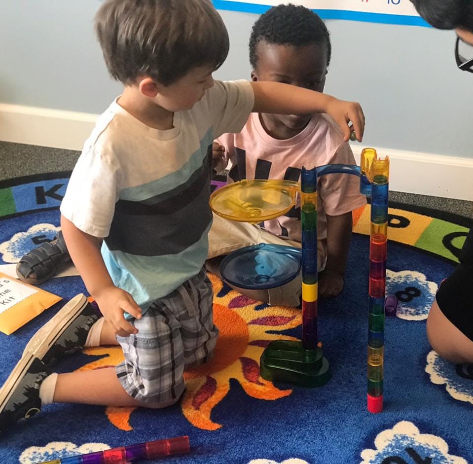 Two children playing with a colorful marble run toy on a blue rug