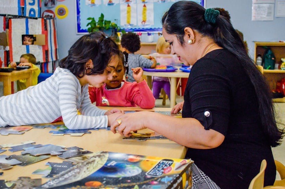 Adult and two children working on a puzzle at a table in a classroom
