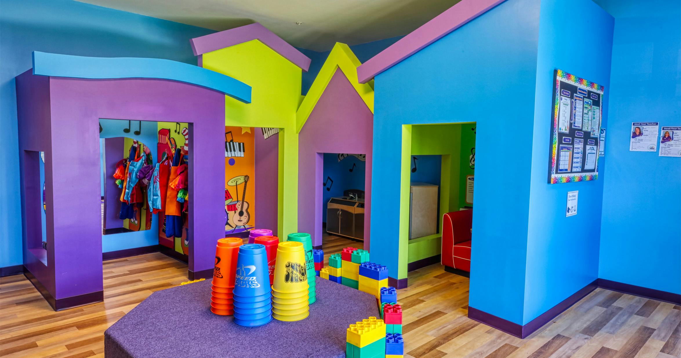 Colorful playroom with house-shaped archways, dress-up clothes, and building blocks