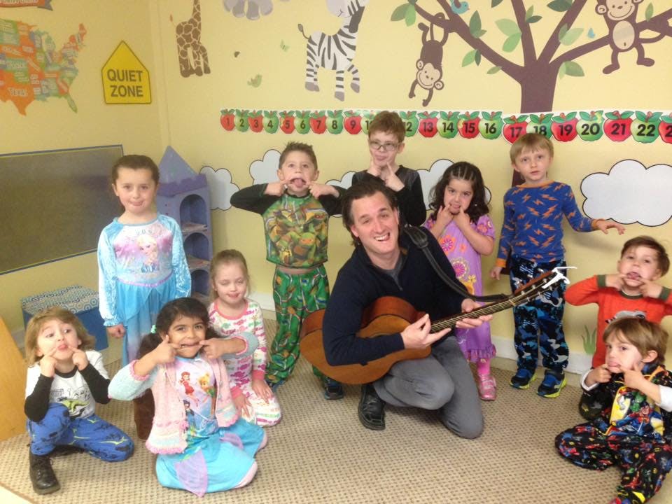 Adult playing guitar with children making funny faces in a classroom