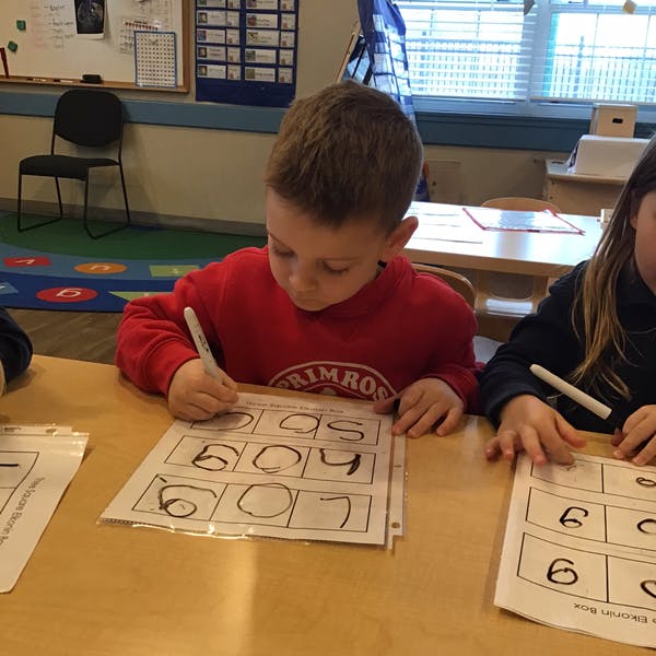 Child writing numbers on a worksheet in a classroom