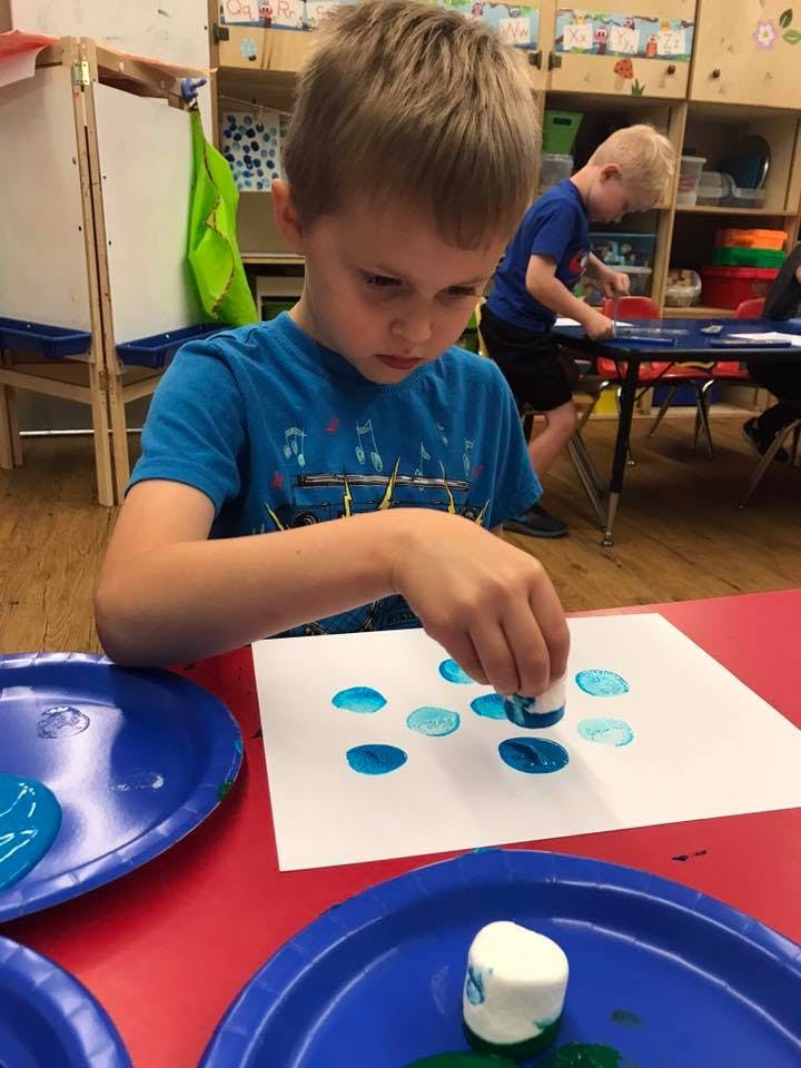 Child making blue paint prints on paper in a classroom