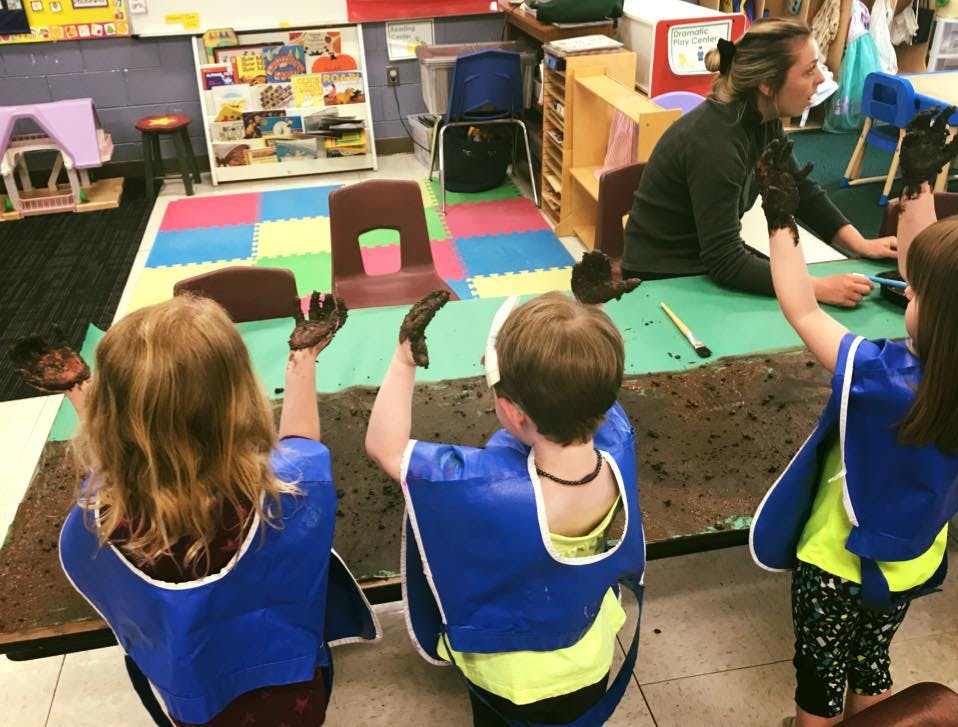 Children with paint on their hands in a classroom with an adult in a classroom