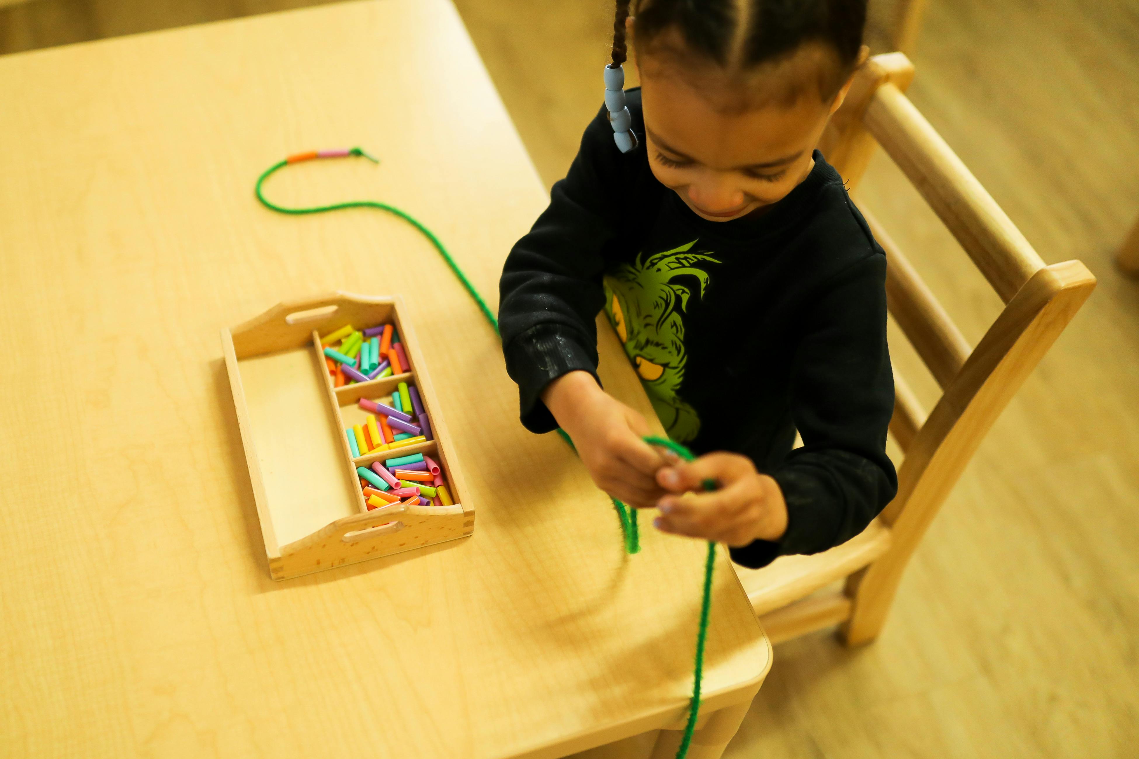 Child stringing beads at a table