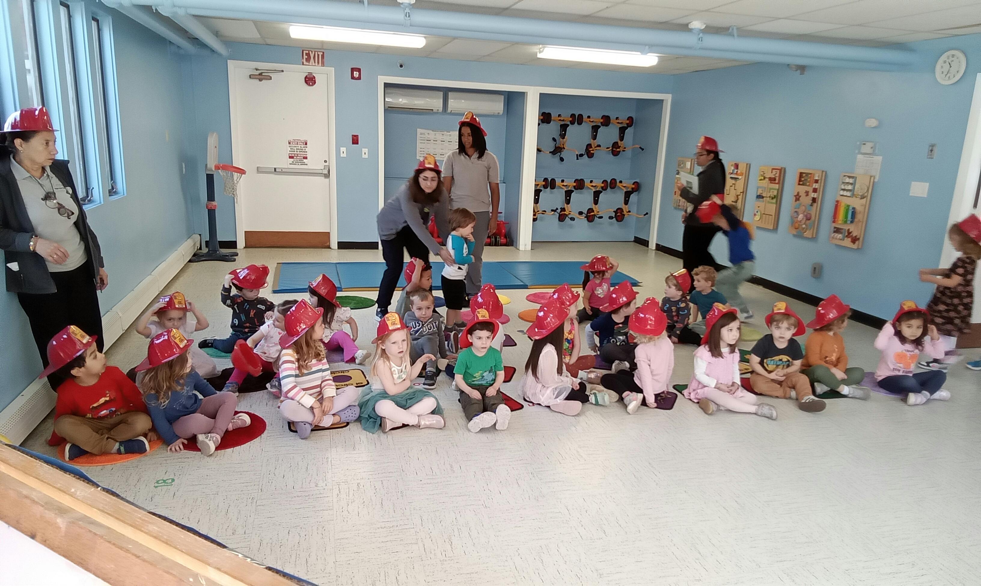 Adults and children in red hats sitting on the floor in a classroom