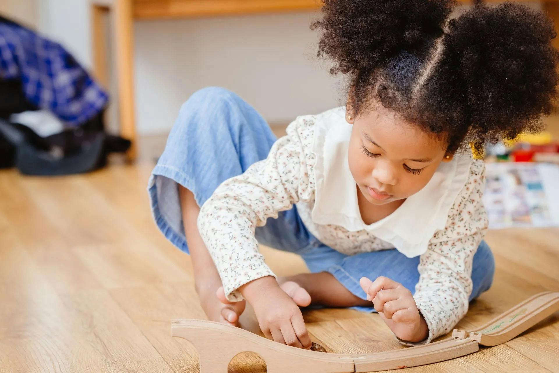 Child sitting on floor playing with wooden train track
