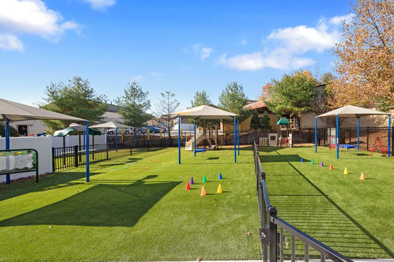 An outdoor playground with artificial turf, play structures, and shade canopies