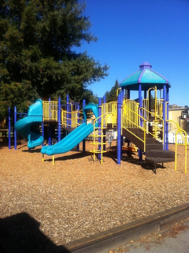 Playground with blue and yellow equipment, slides, and stairs on wood chips