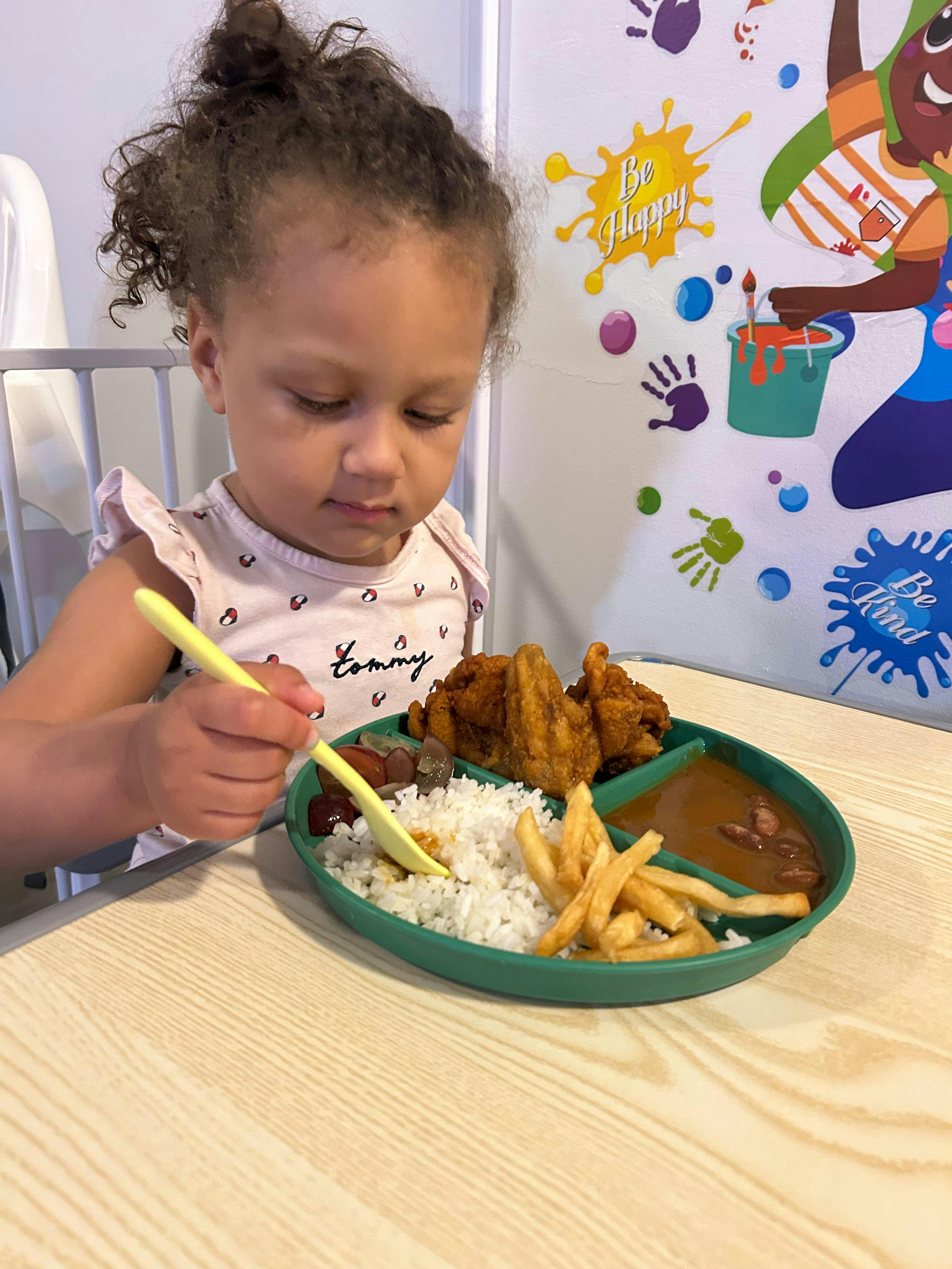 Child eating from a divided plate with rice, chicken, and fries